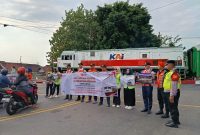 Personel KAI Daop 7 Madiun bentangkan banner saat sosialisasi keselamatan di pintu pelintasan Stasiun Madiun, Jumat (15/8/2025).