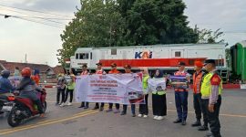 Personel KAI Daop 7 Madiun bentangkan banner saat sosialisasi keselamatan di pintu pelintasan Stasiun Madiun, Jumat (15/8/2025).