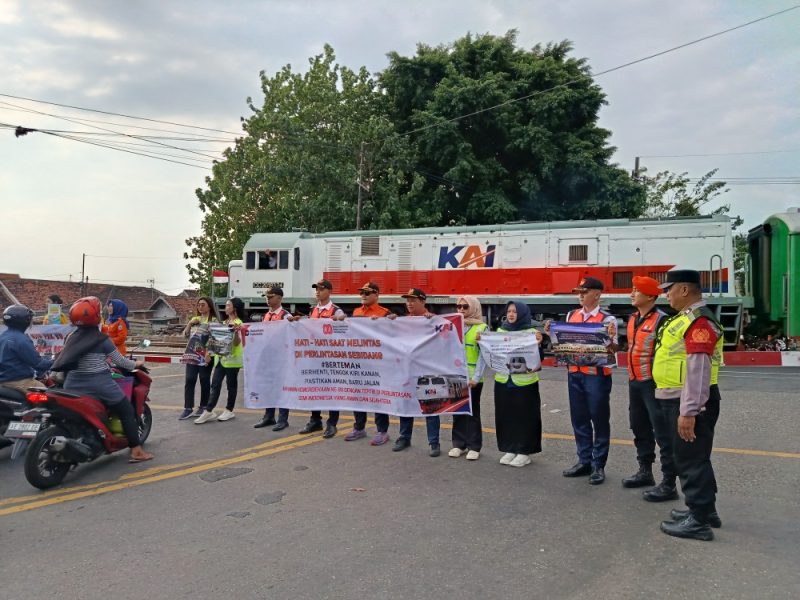 Personel KAI Daop 7 Madiun bentangkan banner saat sosialisasi keselamatan di pintu pelintasan Stasiun Madiun, Jumat (15/8/2025).